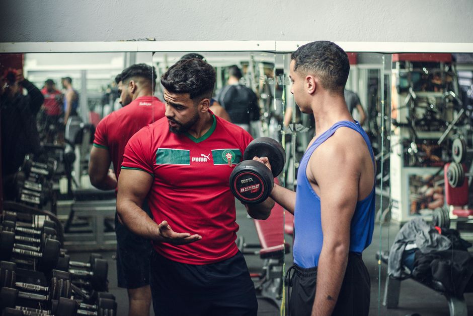 Huấn luyện viên kèm hội viên tập tạ trong phòng gym